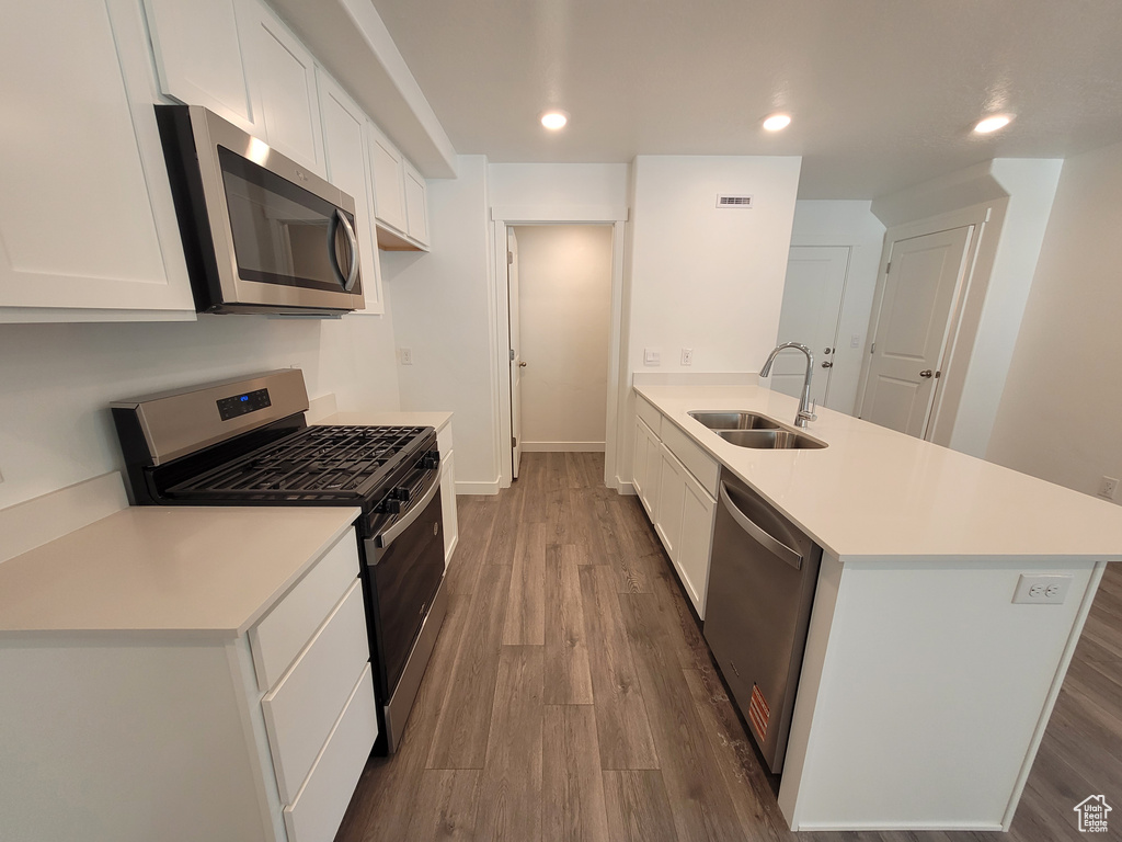 Kitchen featuring appliances with stainless steel finishes, a peninsula, wood finished floors, light countertops, and white cabinets