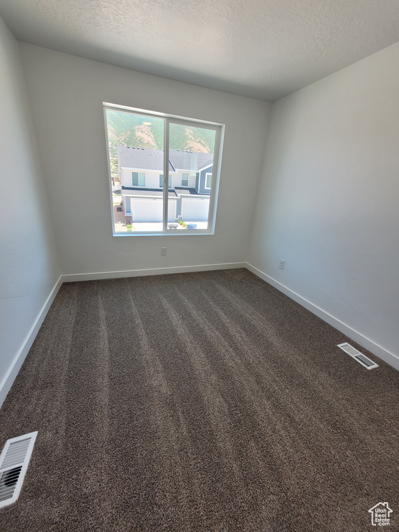 Unfurnished room featuring dark carpet and a textured ceiling