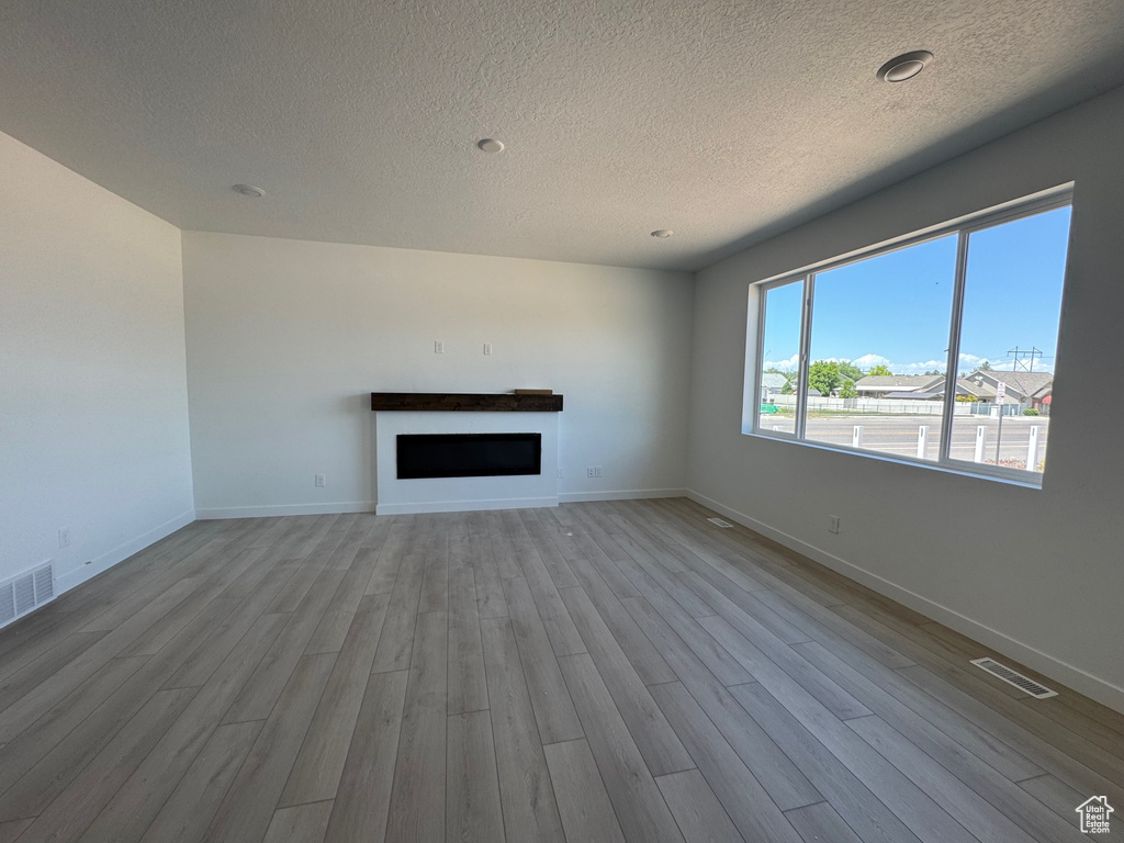 Unfurnished living room featuring a fireplace, a textured ceiling, wood finished floors, and baseboards