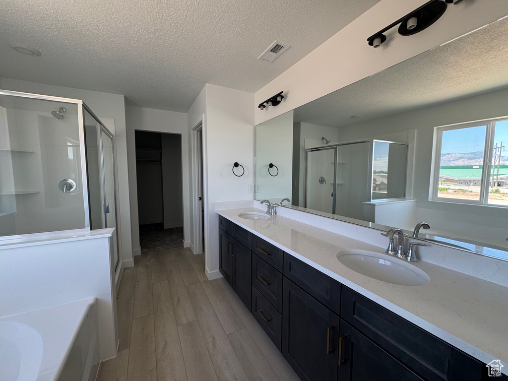 Bathroom with a shower stall, a textured ceiling, a garden tub, wood finished floors, and double vanity