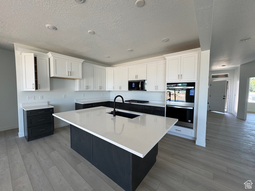 Kitchen with a sink, appliances with stainless steel finishes, a textured ceiling, white cabinetry, and light wood-type flooring