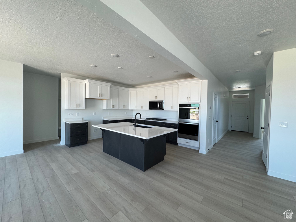 Kitchen featuring a textured ceiling, multiple ovens, a sink, light wood finished floors, and baseboards
