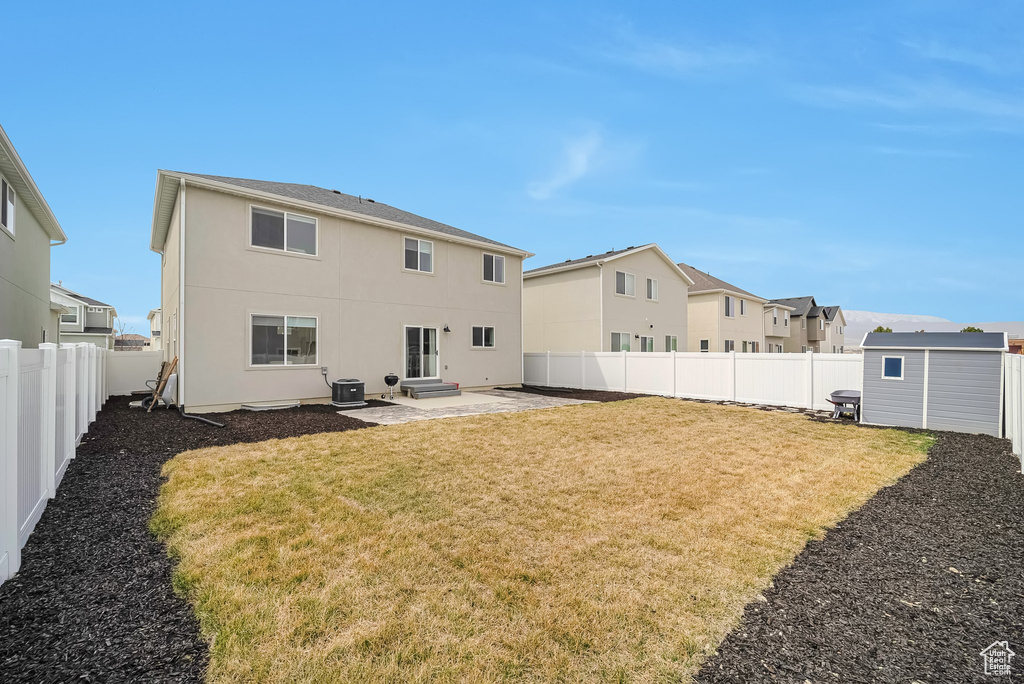 Rear view of property featuring a storage shed, a patio, a fenced backyard, a lawn, and an outbuilding