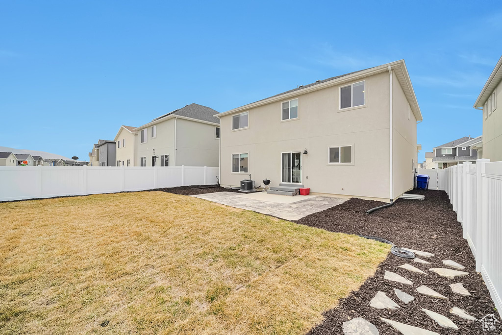 Rear view of property featuring a patio area, stucco siding, a fenced backyard, central AC unit, and a lawn