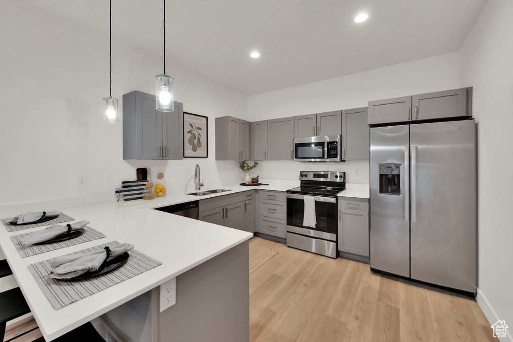 Kitchen with appliances with stainless steel finishes, gray cabinets, a peninsula, a sink, and light countertops
