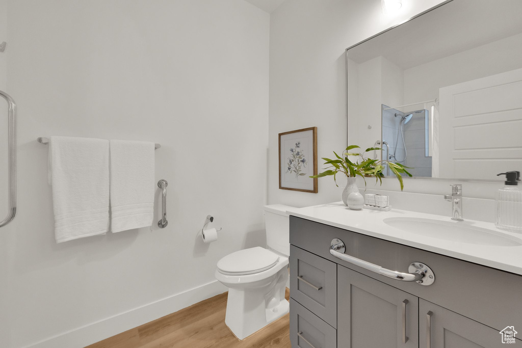 Bathroom with a shower, baseboards, wood finished floors, toilet, and vanity