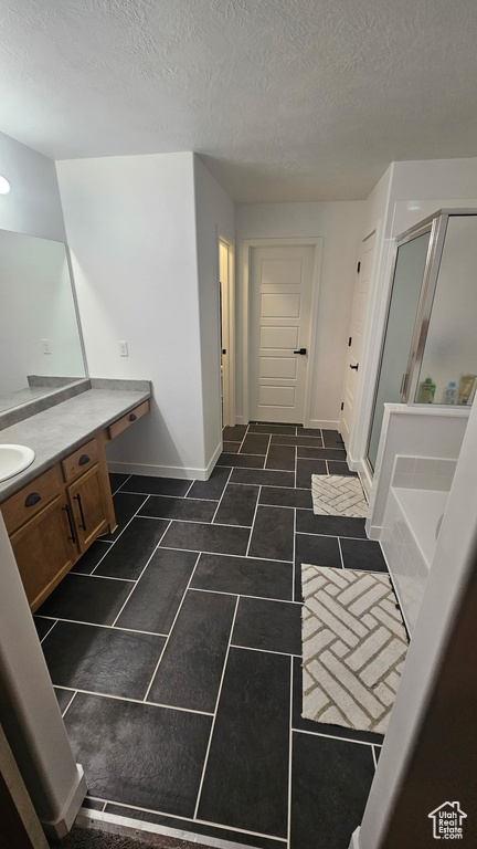 Bathroom featuring vanity, a stall shower, a bath, a textured ceiling, and baseboards