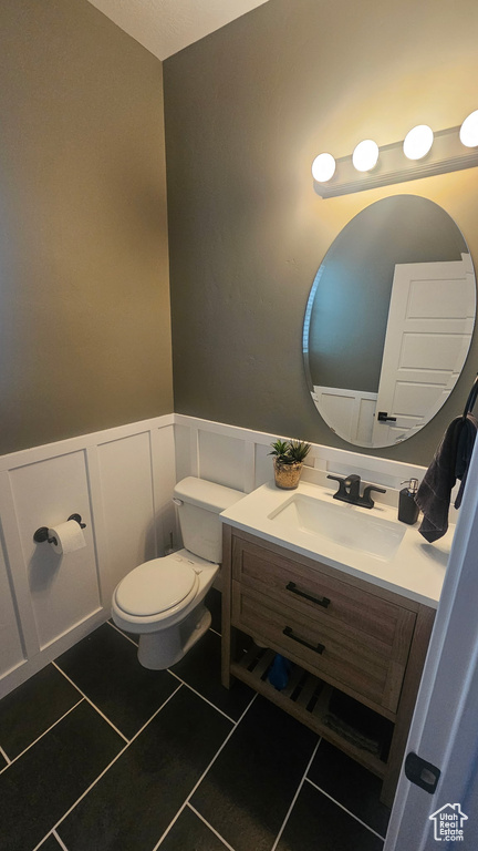 Half bath featuring vanity, tile patterned flooring, wainscoting, toilet, and a decorative wall