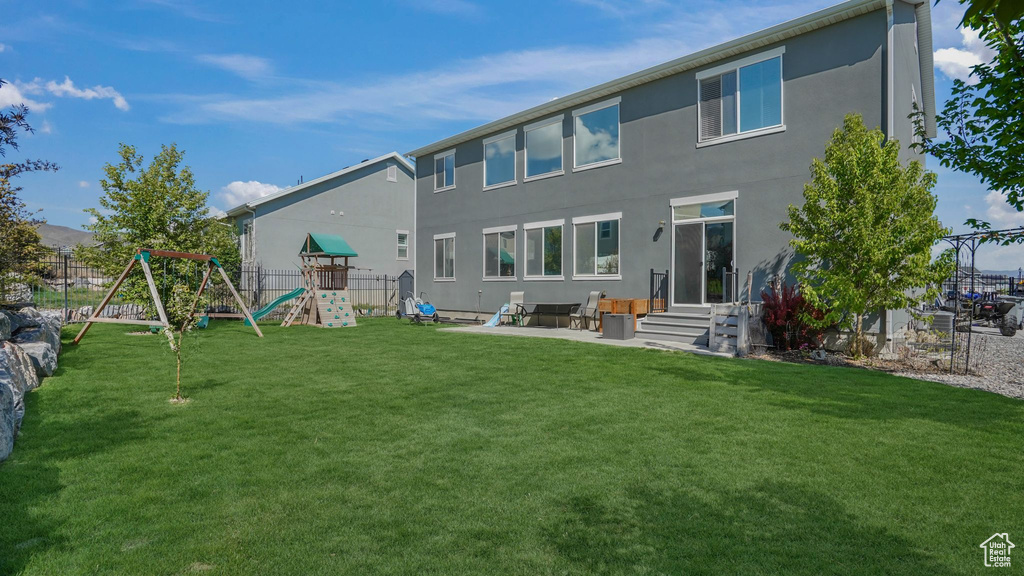 Back of property with a lawn, fence, a playground, a patio, and stucco siding