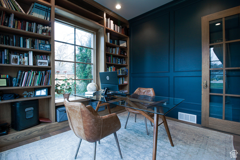 Office area featuring built in features, a decorative wall, visible vents, and wood finished floors