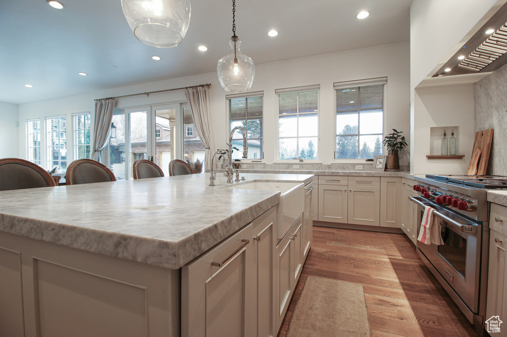 Kitchen with wall chimney range hood, a center island with sink, designer range, and recessed lighting