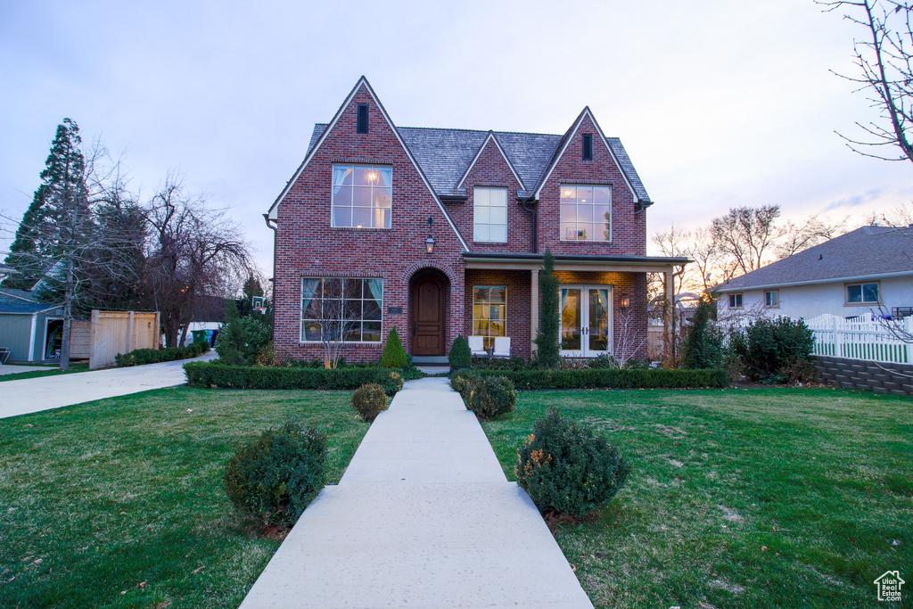 Tudor house featuring brick siding, fence, and a front lawn