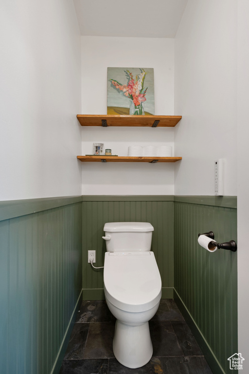 Bathroom with a wainscoted wall, stone tile floors, and toilet