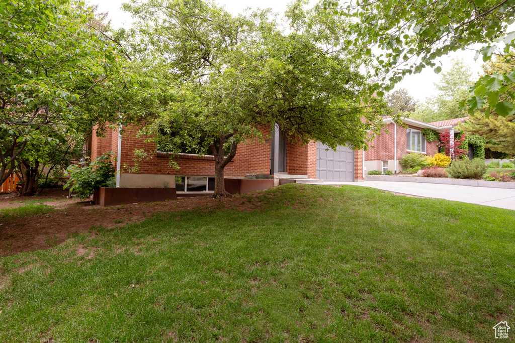 View of front of house with driveway, brick siding, a front yard, and an attached garage
