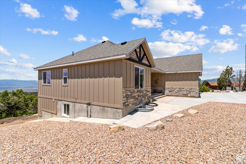 View of property exterior featuring a shingled roof, stone siding, board and batten siding, and a patio