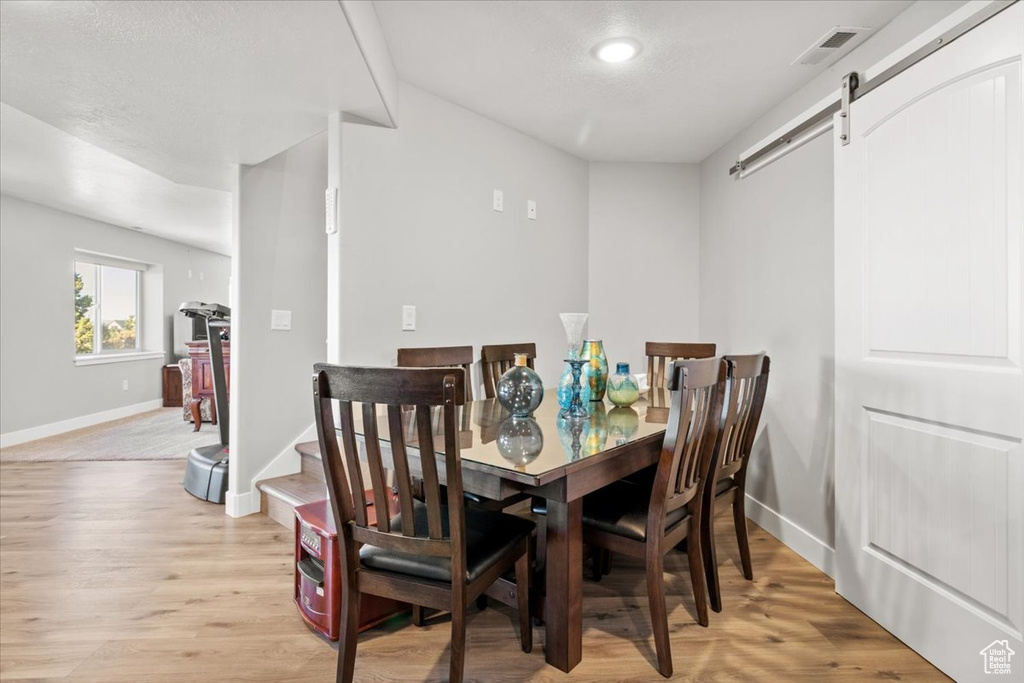 Dining area with a barn door, baseboards, light wood-style flooring, stairs, and recessed lighting