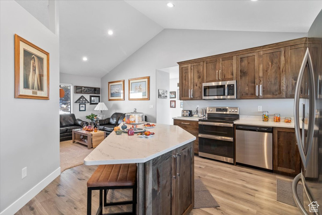 Kitchen with appliances with stainless steel finishes, light wood-type flooring, a kitchen island, open floor plan, and dark brown cabinetry