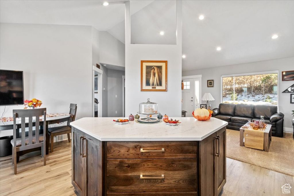 Kitchen with lofted ceiling, open floor plan, light wood finished floors, a center island, and light stone counters