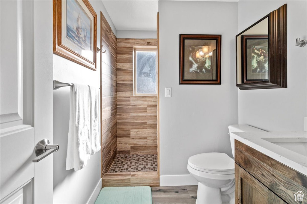 Bathroom featuring a tile shower, vanity, toilet, baseboards, and wood finished floors