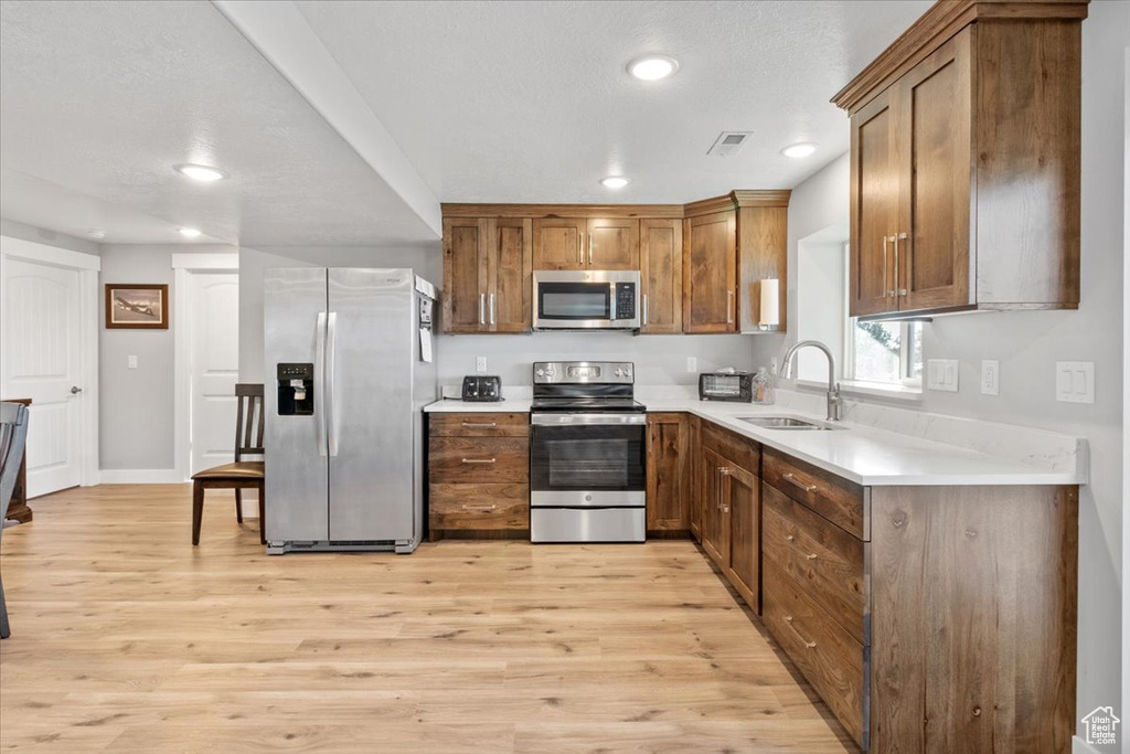 Kitchen featuring appliances with stainless steel finishes, a sink, recessed lighting, light countertops, and light wood-type flooring