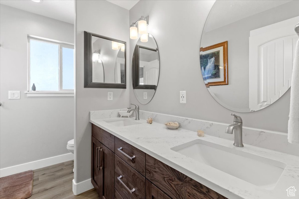 Full bath featuring toilet, double vanity, baseboards, and wood finished floors