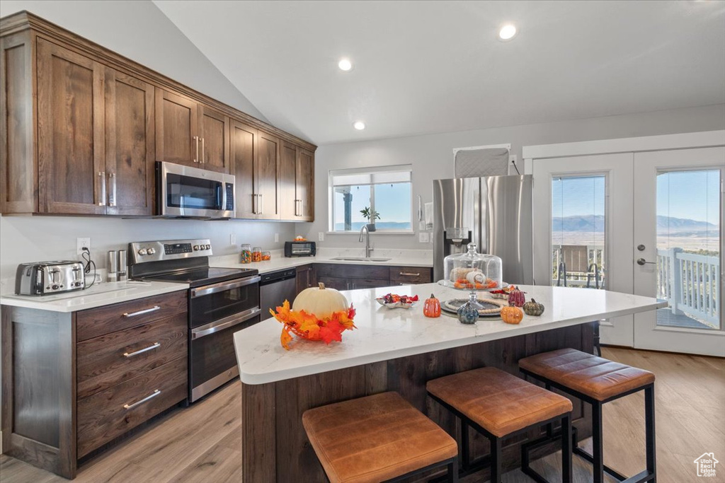 Kitchen featuring appliances with stainless steel finishes, a breakfast bar, light countertops, a sink, and light wood-type flooring