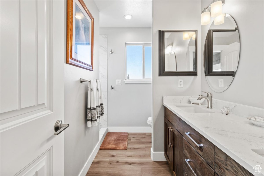 Full bath featuring double vanity, a shower, wood finished floors, baseboards, and toilet