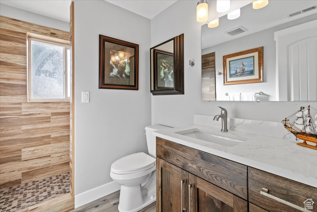 Bathroom with vanity, tiled shower, toilet, baseboards, and wood finished floors