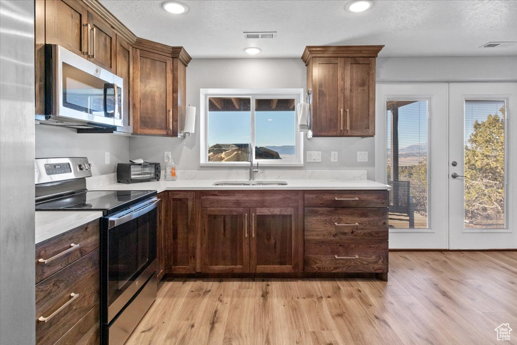 Kitchen with stainless steel appliances, a sink, french doors, light wood-type flooring, and a textured ceiling