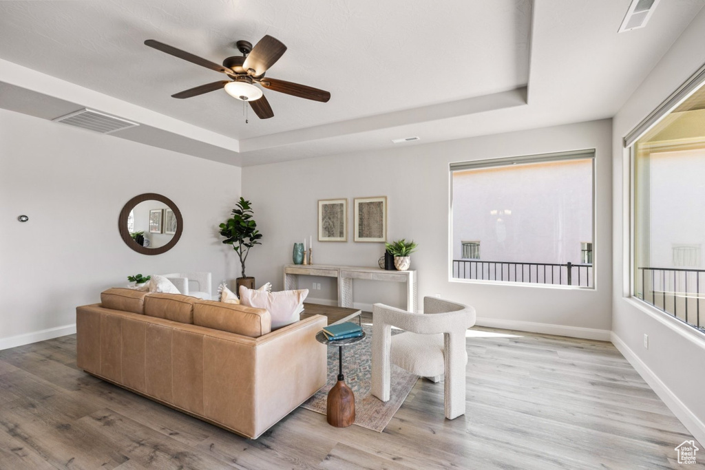 Living area featuring a tray ceiling, a ceiling fan, light wood-style floors, and baseboards