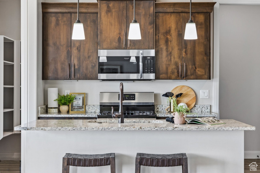 Kitchen featuring stainless steel appliances, an island with sink, dark brown cabinetry, a kitchen bar, and a sink