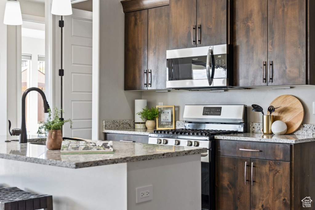 Kitchen featuring stainless steel appliances, dark brown cabinets, light stone counters, a kitchen bar, and decorative light fixtures