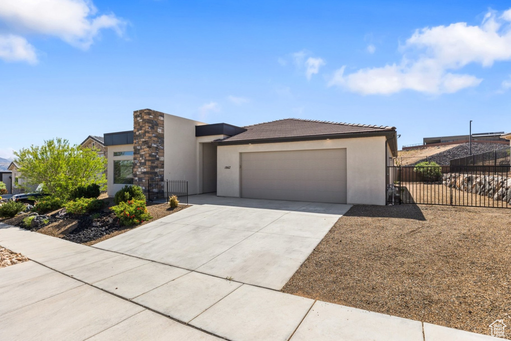 View of front facade with stucco siding, fence, driveway, an attached garage, and a tile roof