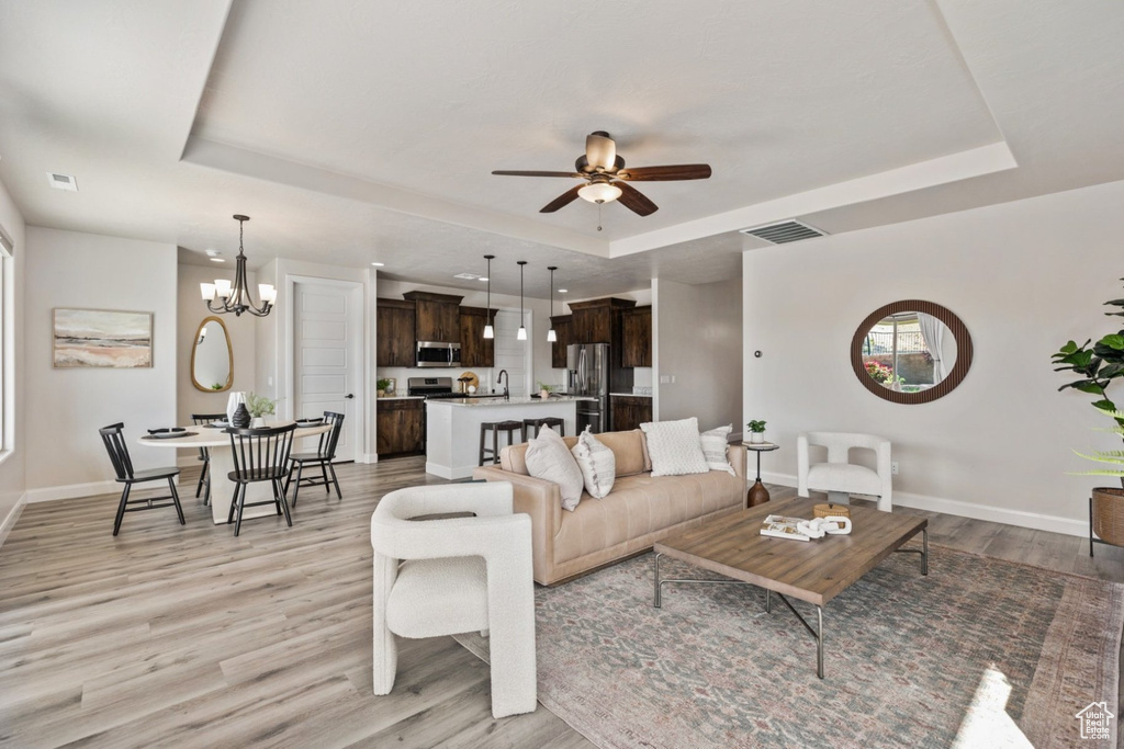 Living area featuring a raised ceiling, light wood finished floors, baseboards, and ceiling fan