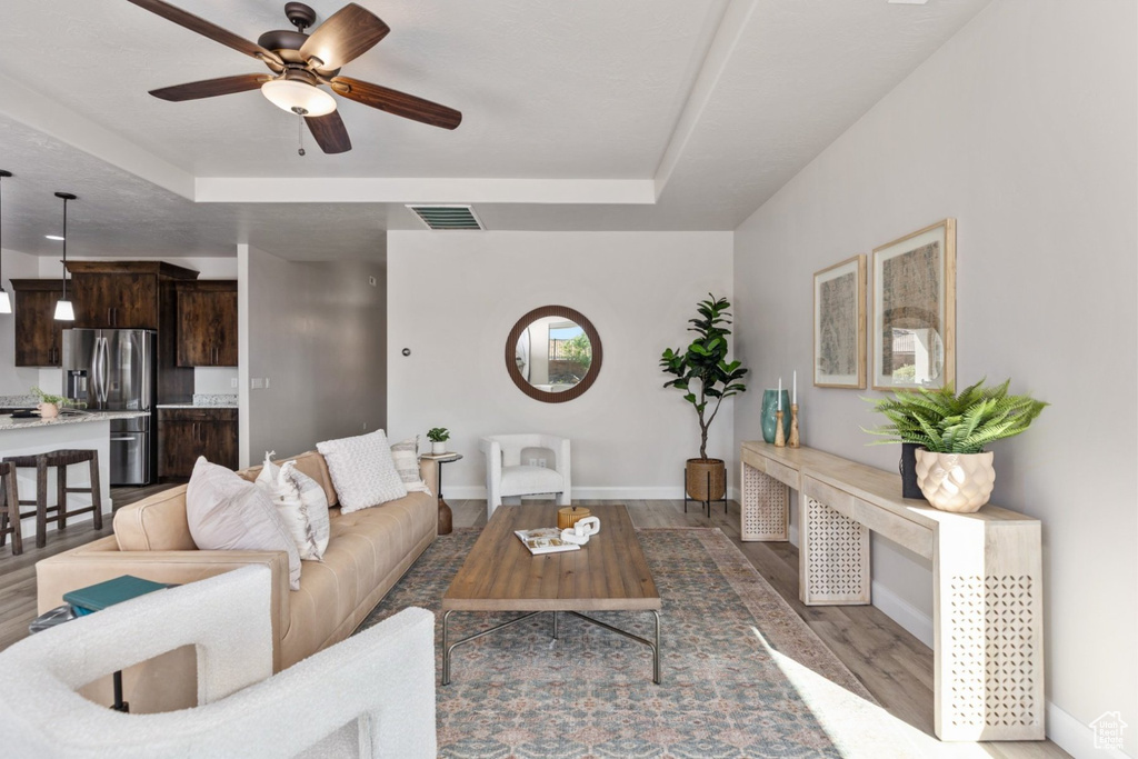 Living area featuring a tray ceiling, a ceiling fan, baseboards, and wood finished floors