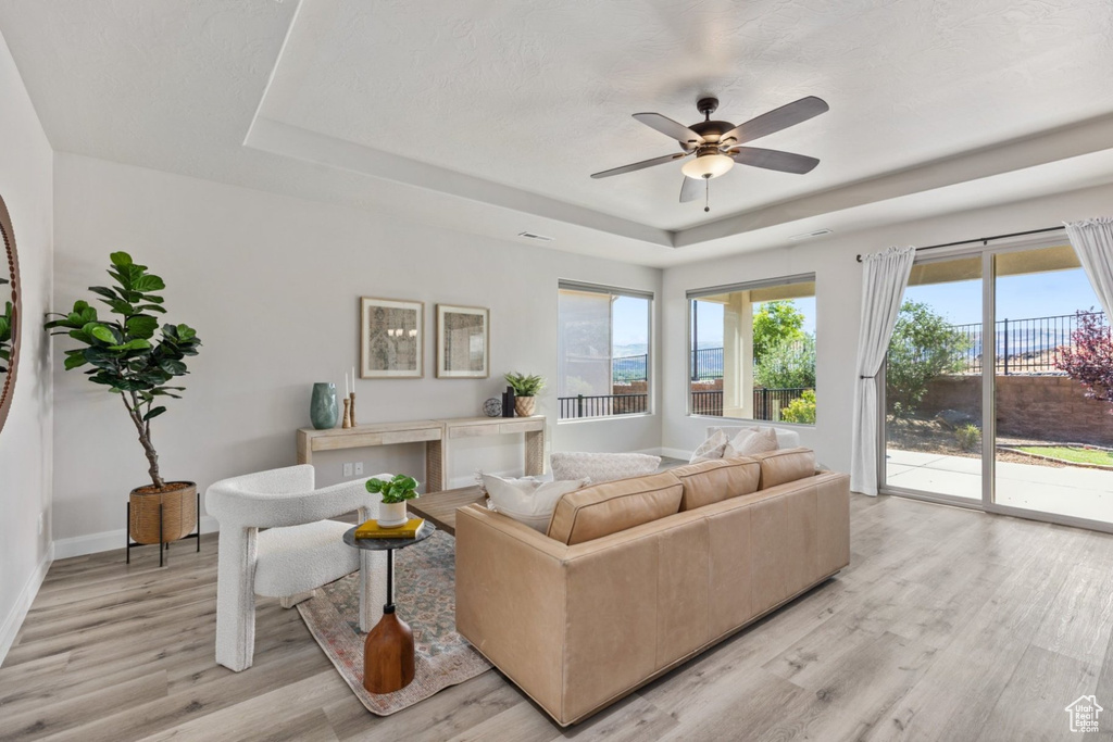 Living room featuring a tray ceiling, light wood-style flooring, ceiling fan, and baseboards