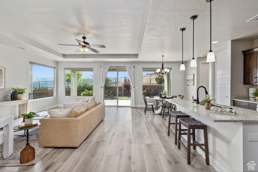 Living area featuring light wood-style floors, healthy amount of natural light, ceiling fan, a chandelier, and a textured ceiling