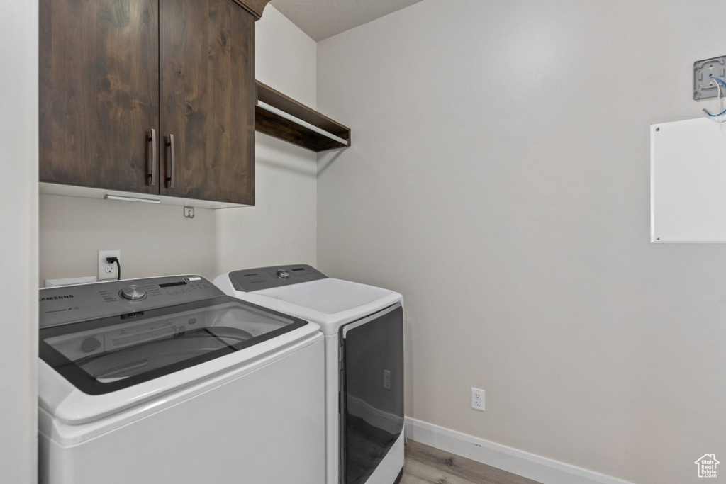 Washroom featuring independent washer and dryer, cabinet space, light wood finished floors, and baseboards