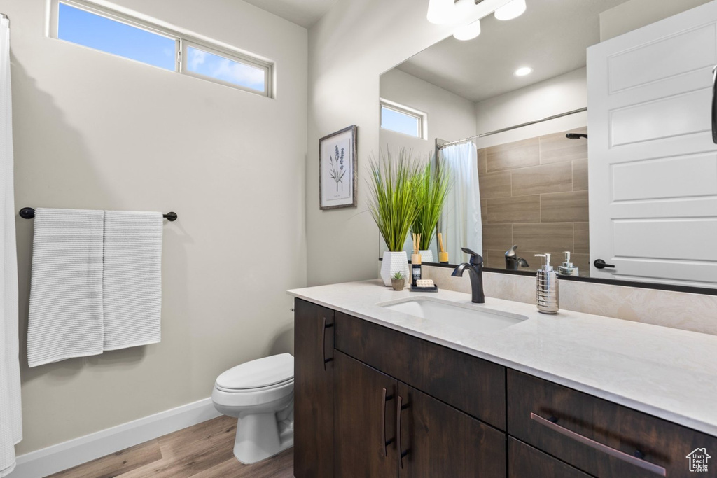 Full bath with wood finished floors, baseboards, toilet, vanity, and a shower with shower curtain