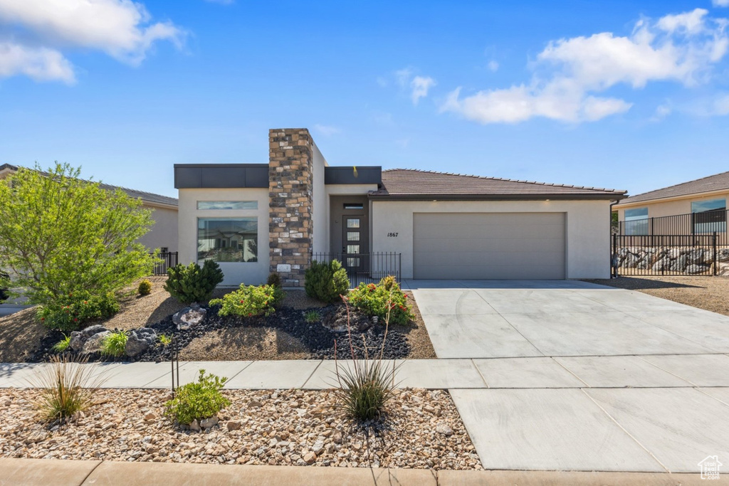 View of front of house featuring stucco siding, driveway, a garage, and fence