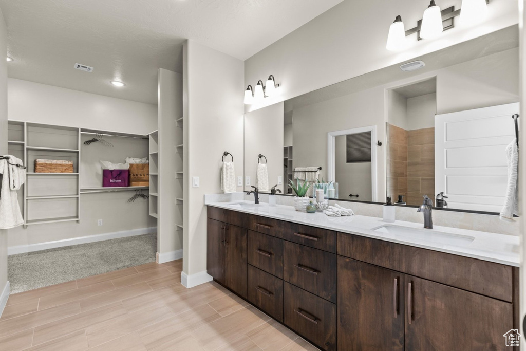 Bathroom featuring a spacious closet, double vanity, baseboards, a tile shower, and wood finished floors