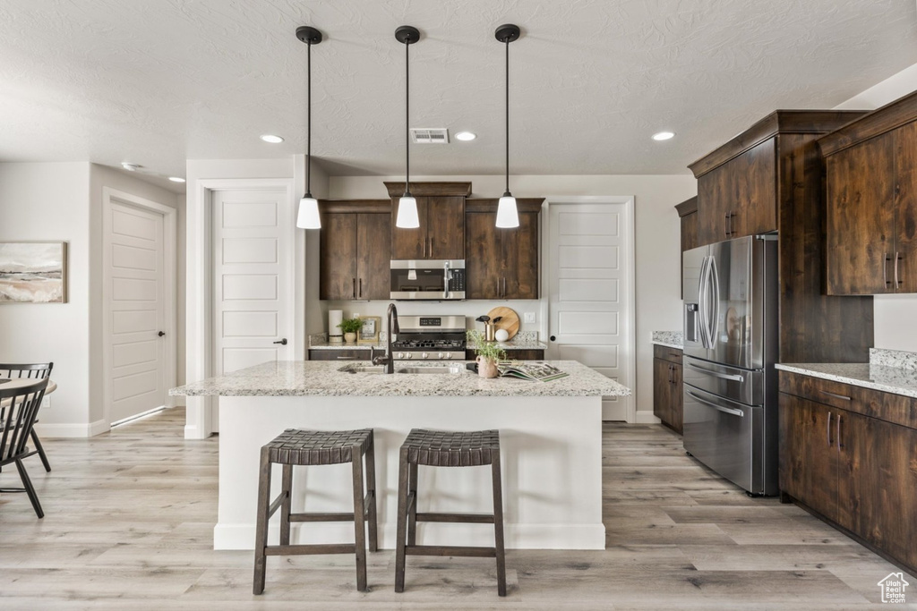 Kitchen featuring stainless steel appliances, a sink, light wood-style flooring, dark brown cabinetry, and a breakfast bar