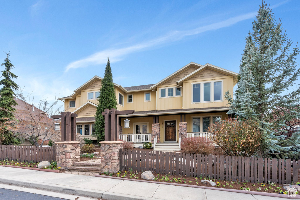 Craftsman-style home featuring a fenced front yard, covered porch, and stone siding