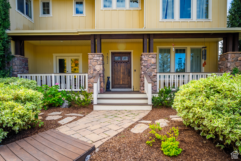 View of exterior entry with covered porch, stone siding, and board and batten siding