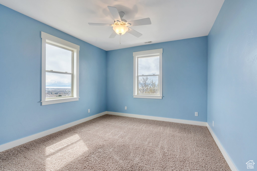 Carpeted spare room featuring baseboards, visible vents, a ceiling fan, and plenty of natural light