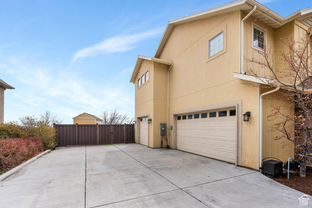 View of side of home with stucco siding, a garage, concrete driveway, and fence