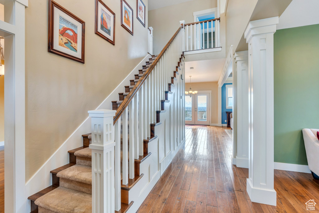 Stairway featuring baseboards, a towering ceiling, decorative columns, hardwood / wood-style floors, and a notable chandelier