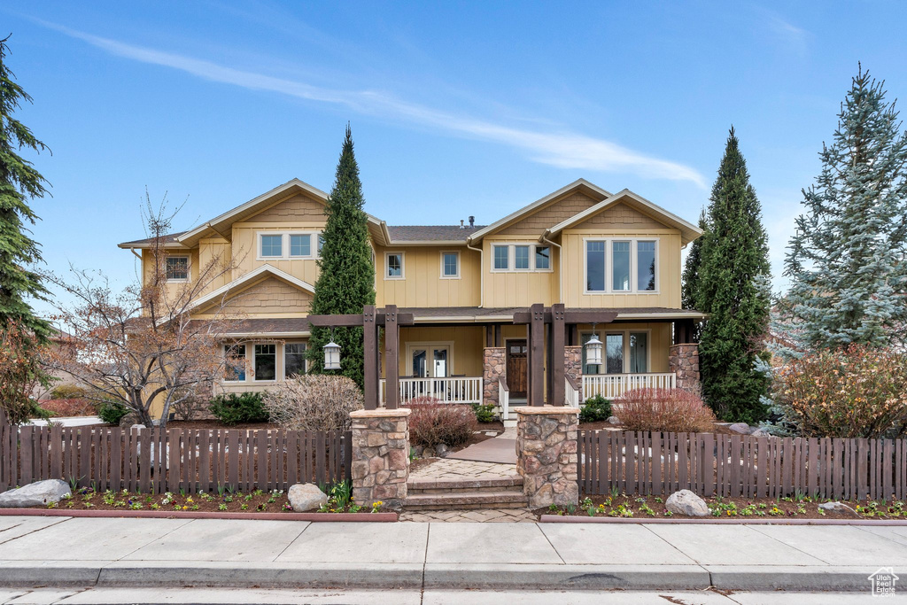 Craftsman inspired home with a fenced front yard, a porch, and stone siding