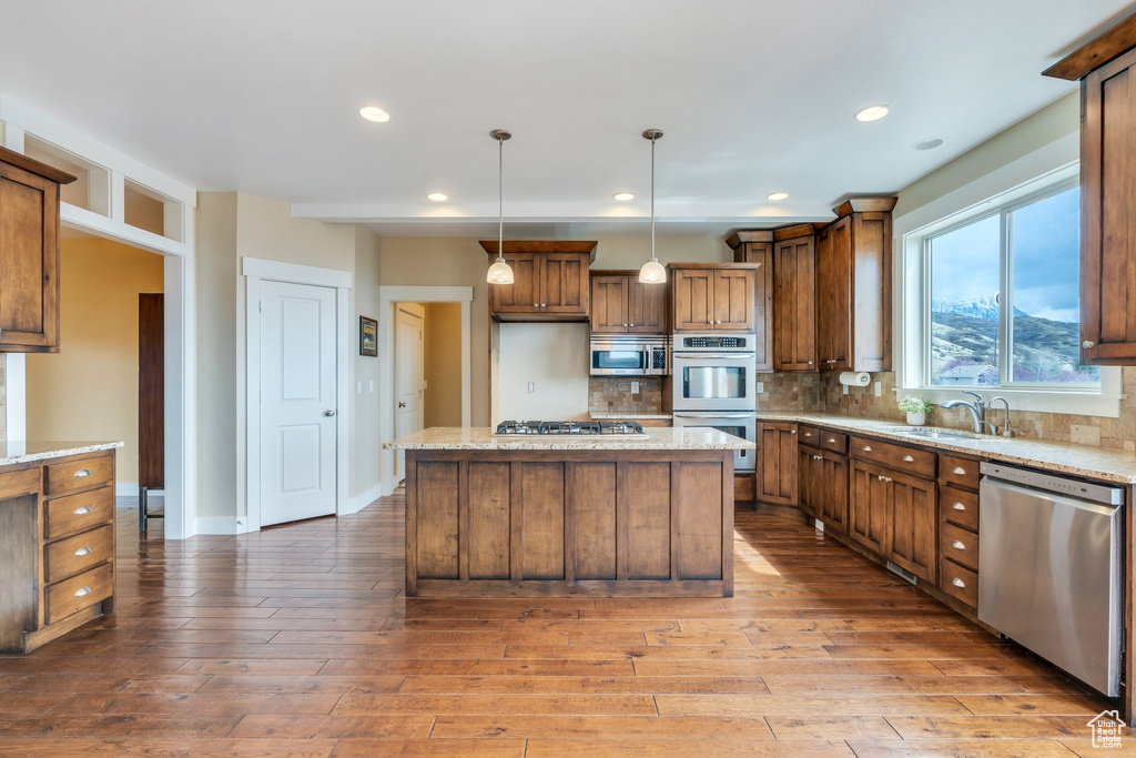 Kitchen with backsplash, a kitchen island, appliances with stainless steel finishes, brown cabinets, and light wood-style flooring