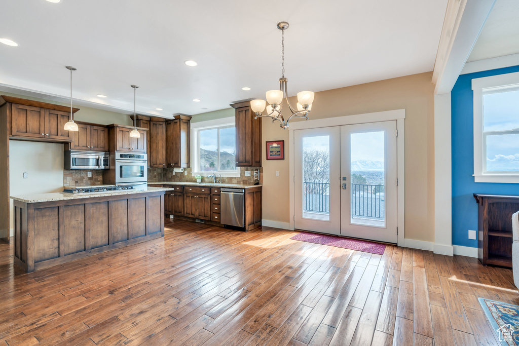 Kitchen featuring backsplash, a chandelier, wood finished floors, stainless steel appliances, and baseboards